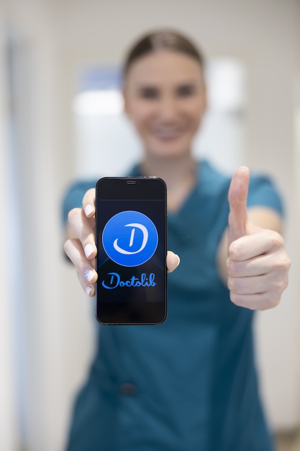 Praxismitarbeiterin hält Smartphone & Daumen hoch in die Kamera für digitale Services und Terminorganisation. Zahnarztpraxis Markt 16 in Leipzig, Dr. med. Franziska Höhne